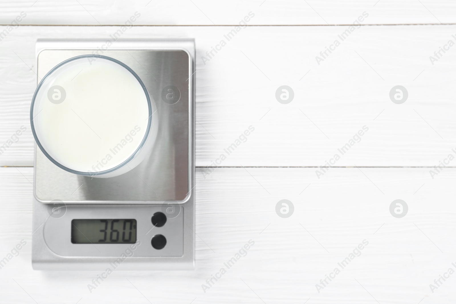 Photo of Kitchen scale with glass of milk on white wooden table, top view. Space for text