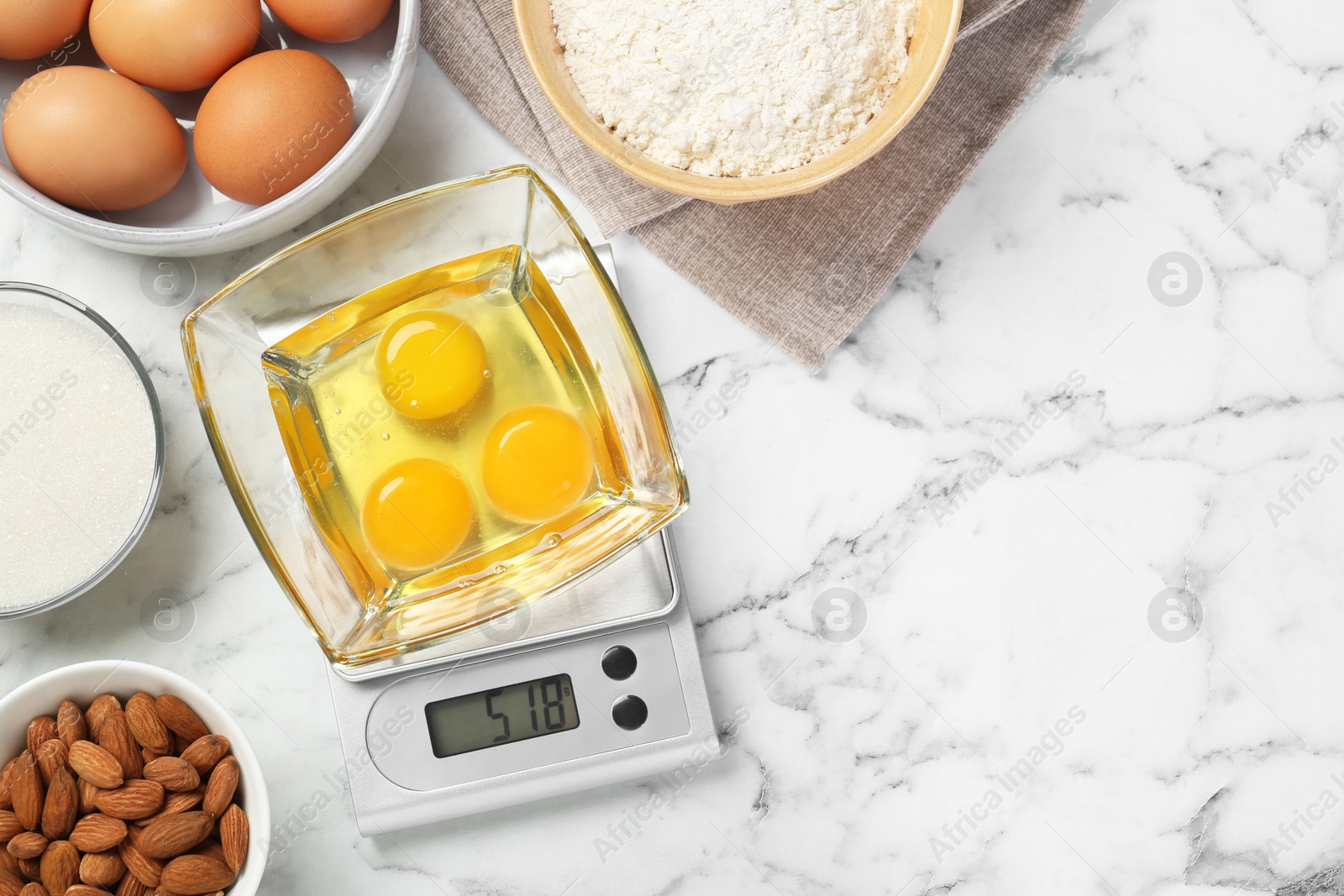 Photo of Flat lay composition of kitchen scale with bowl of raw eggs on white marble table