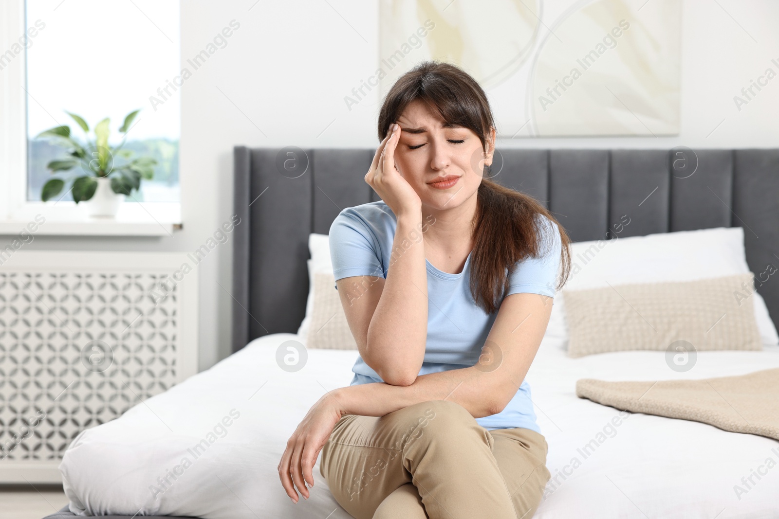 Photo of Upset woman suffering from headache on bed at home