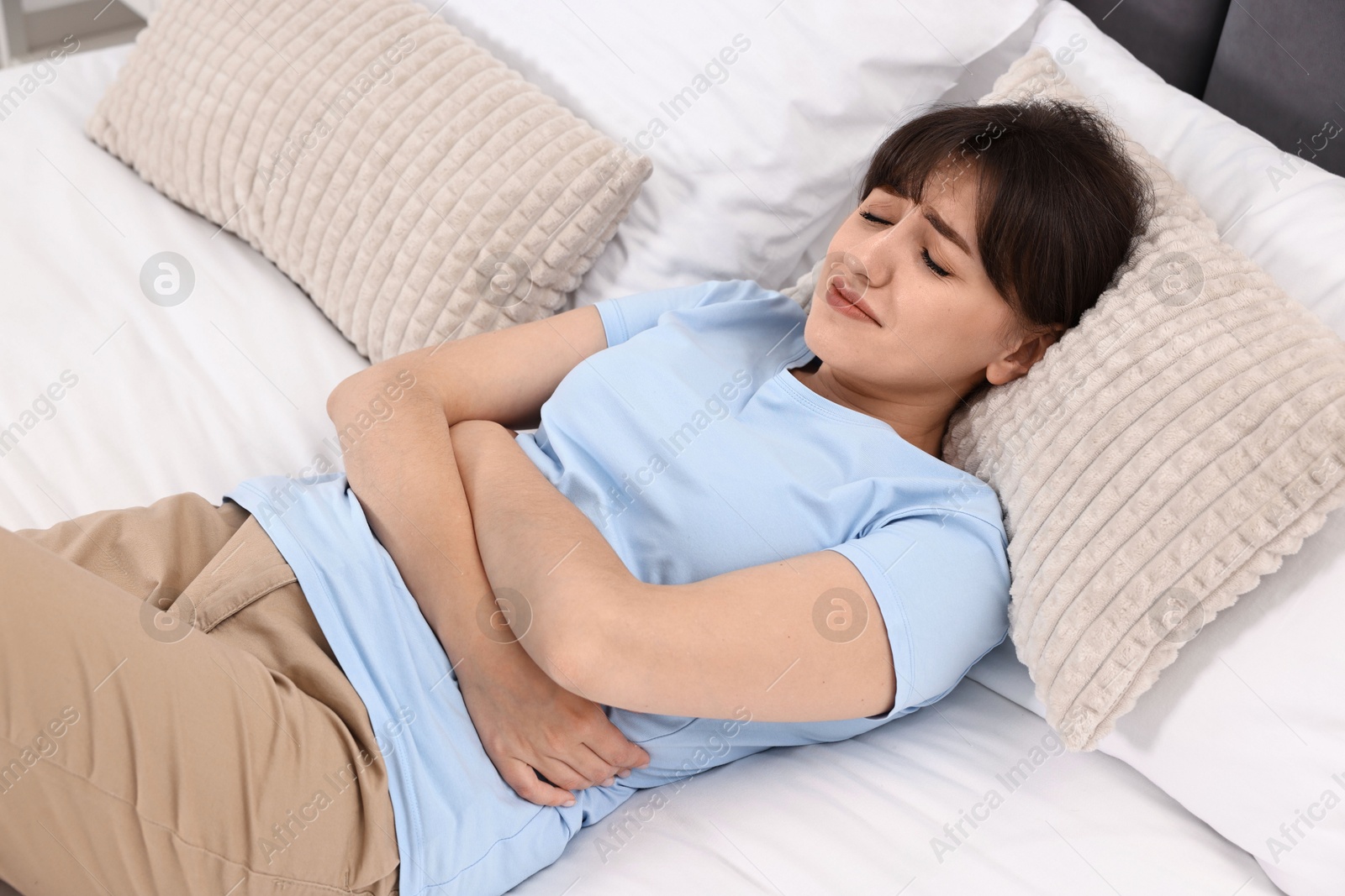 Photo of Upset woman suffering from abdominal pain on bed at home