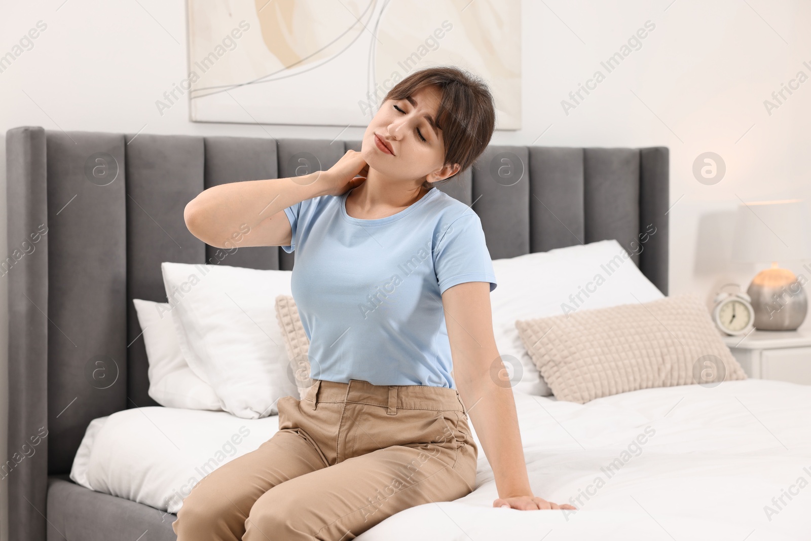 Photo of Upset woman suffering from neck pain on bed at home