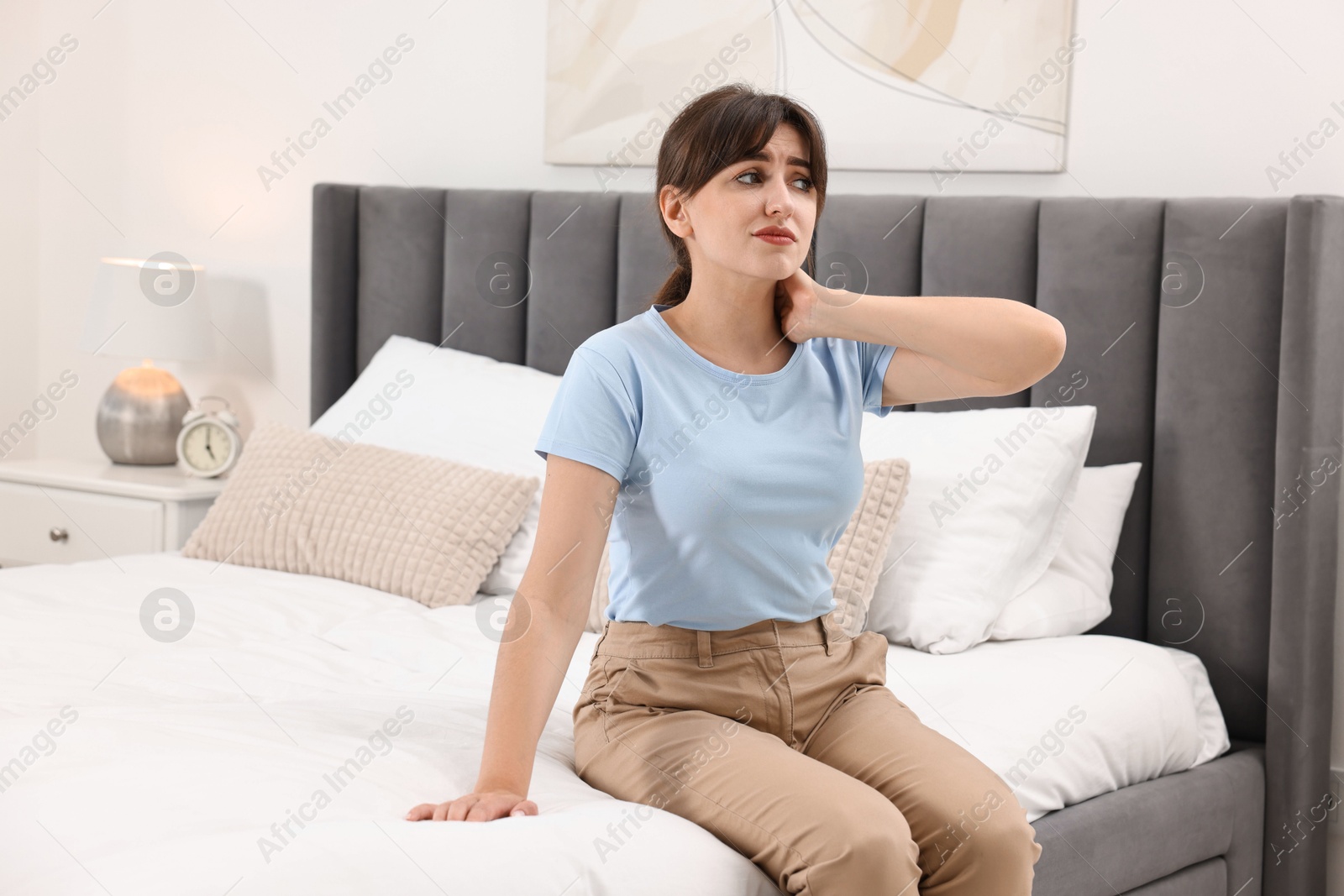 Photo of Upset woman suffering from neck pain on bed at home