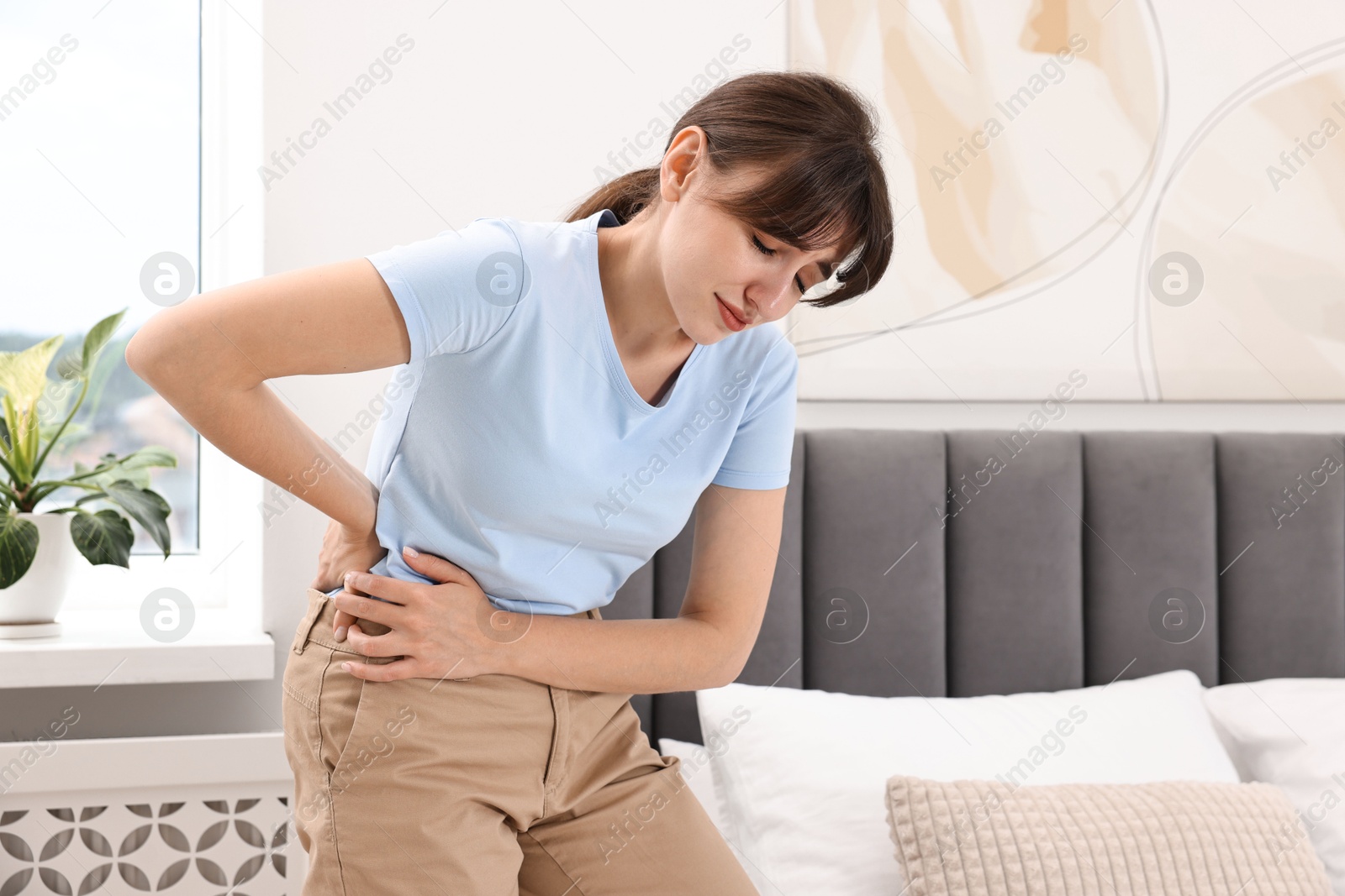 Photo of Upset woman suffering from back pain in bedroom