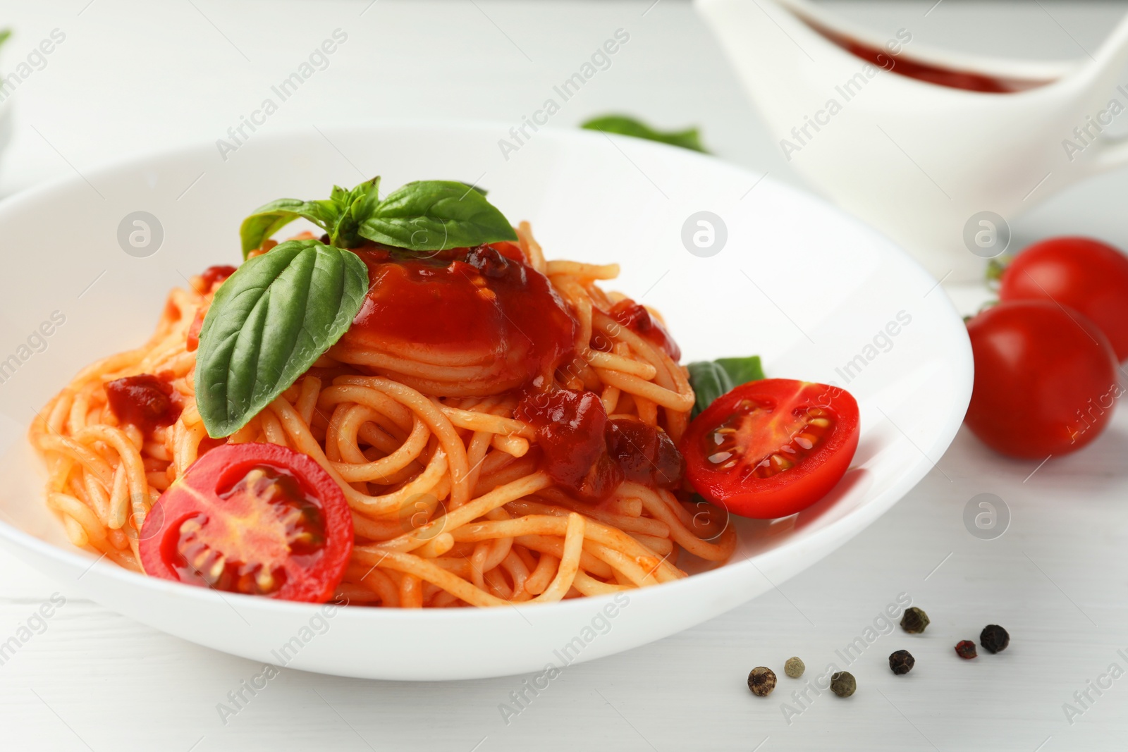 Photo of Delicious pasta with tomato sauce, peppercorns, vegetables and basil on white wooden table, closeup