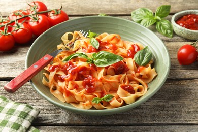 Photo of Delicious pasta with tomato sauce, basil and fork in bowl on wooden table, closeup