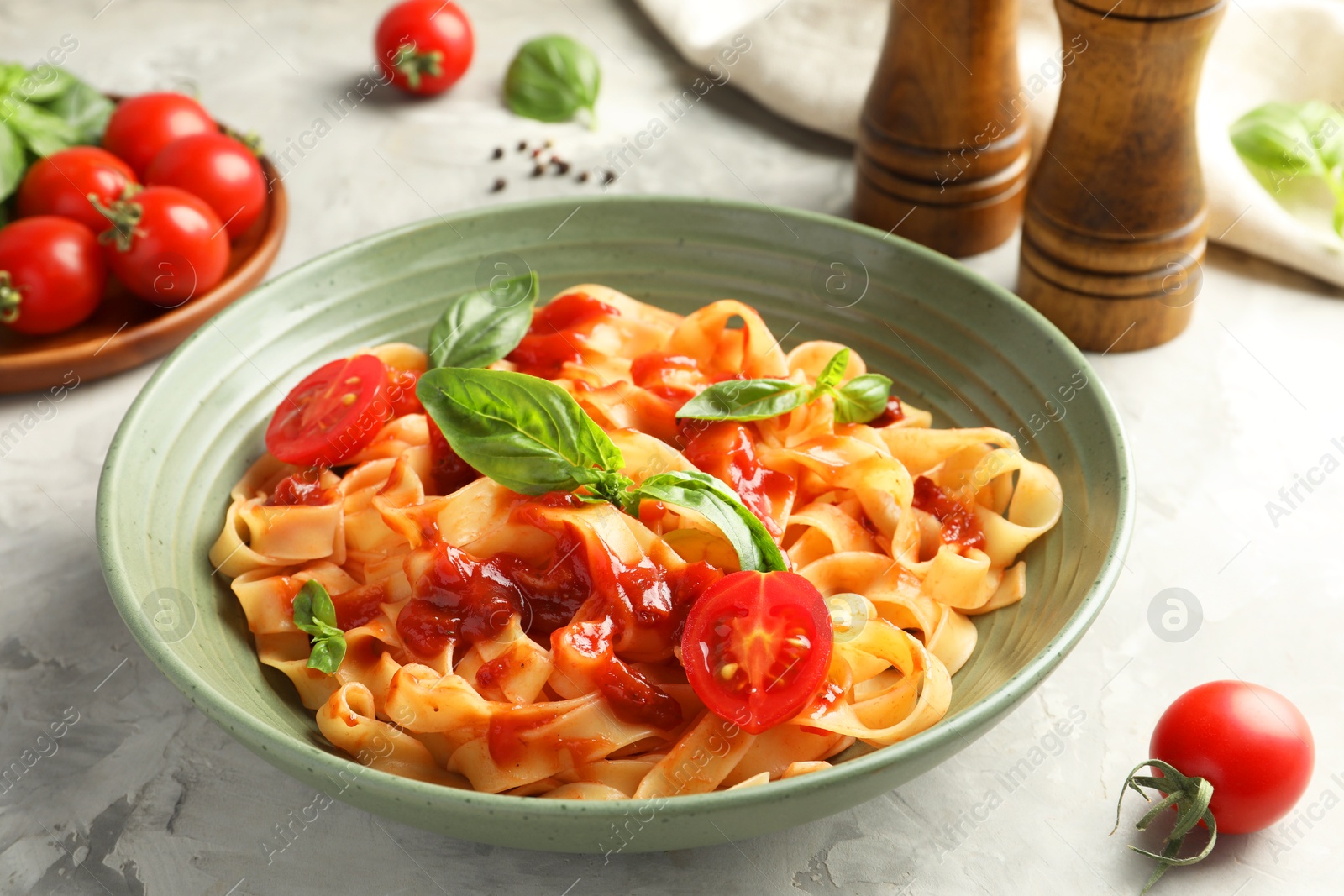 Photo of Delicious pasta with tomato sauce and basil in bowl on grey textured table, closeup