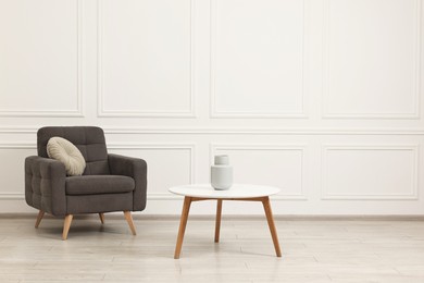 Soft armchair, coffee table and vase in stylish room. Space for text