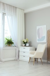 Photo of Soft armchair, chest of drawers, houseplant and window with curtains in room. Interior design