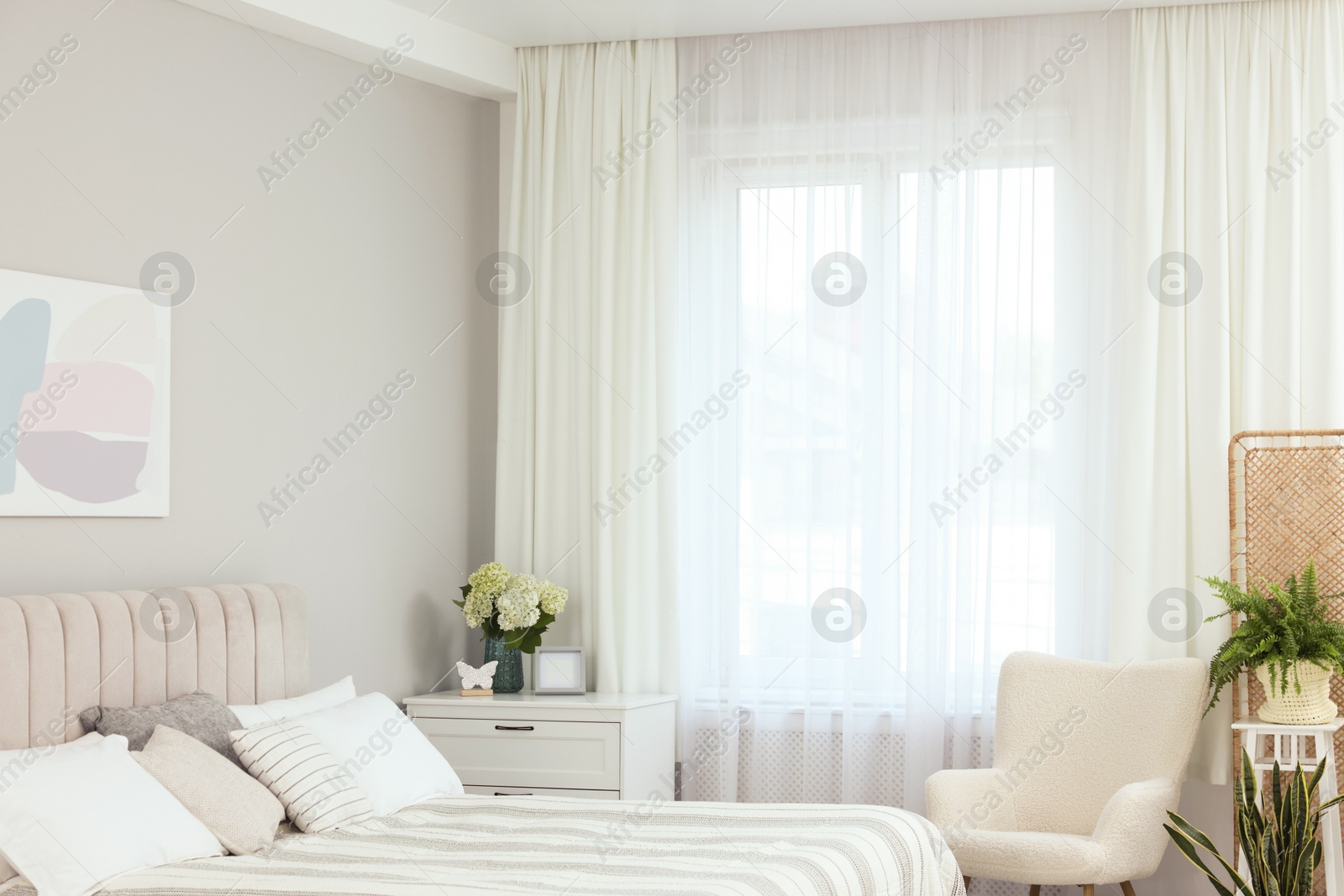 Photo of Large bed, chest of drawers, armchair, houseplants and window with curtains in bedroom. Interior design