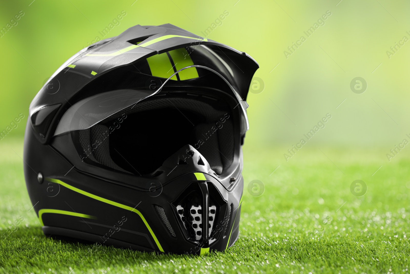 Photo of Modern motorcycle helmet with visor on green grass, closeup. Space for text