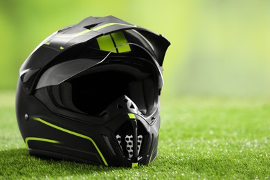 Photo of Modern motorcycle helmet with visor on green grass, closeup. Space for text