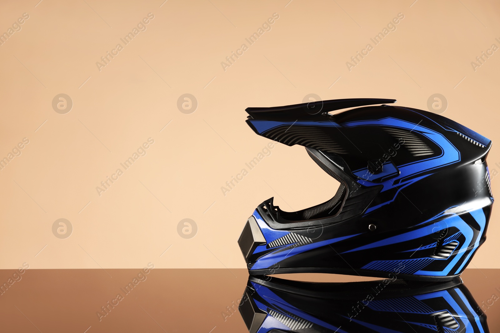 Photo of Modern motorcycle helmet with visor on mirror surface against beige background. Space for text