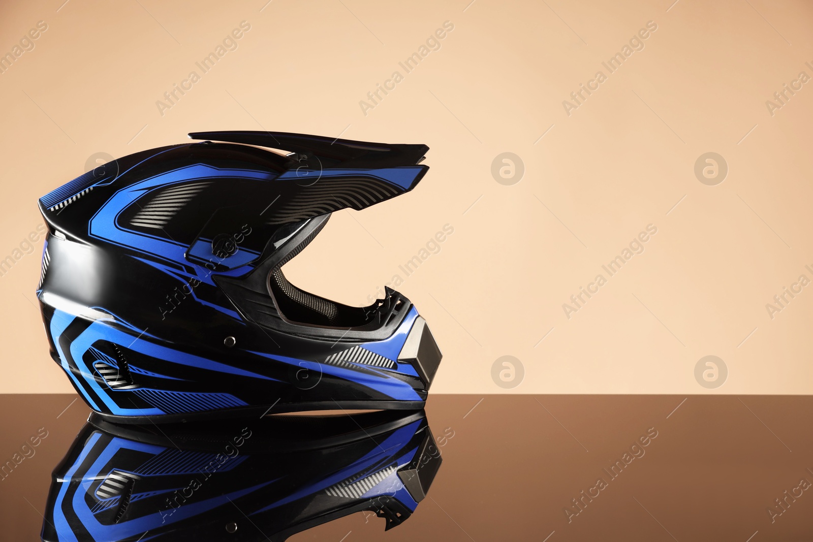 Photo of Modern motorcycle helmet with visor on mirror surface against beige background. Space for text