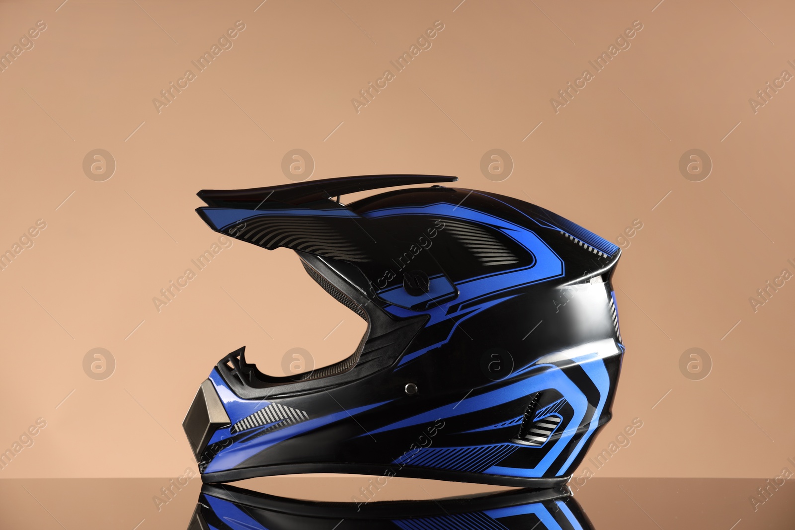 Photo of Modern motorcycle helmet with visor on mirror surface against beige background