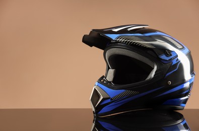 Photo of Modern motorcycle helmet with visor on mirror surface against beige background. Space for text