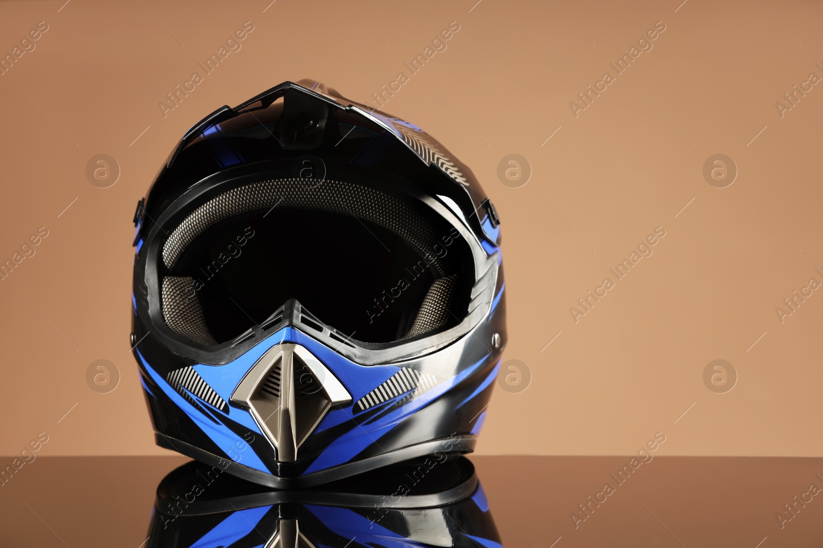 Photo of Modern motorcycle helmet with visor on mirror surface against beige background. Space for text