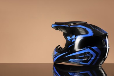 Photo of Modern motorcycle helmet with visor on mirror surface against beige background. Space for text