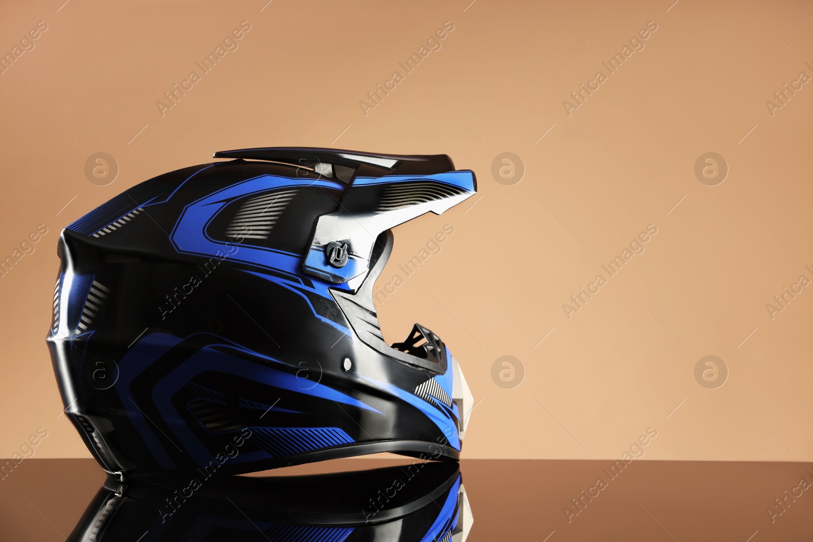 Photo of Modern motorcycle helmet with visor on mirror surface against beige background. Space for text