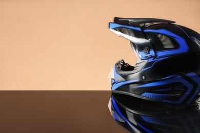 Photo of Modern motorcycle helmet with visor on mirror surface against beige background. Space for text