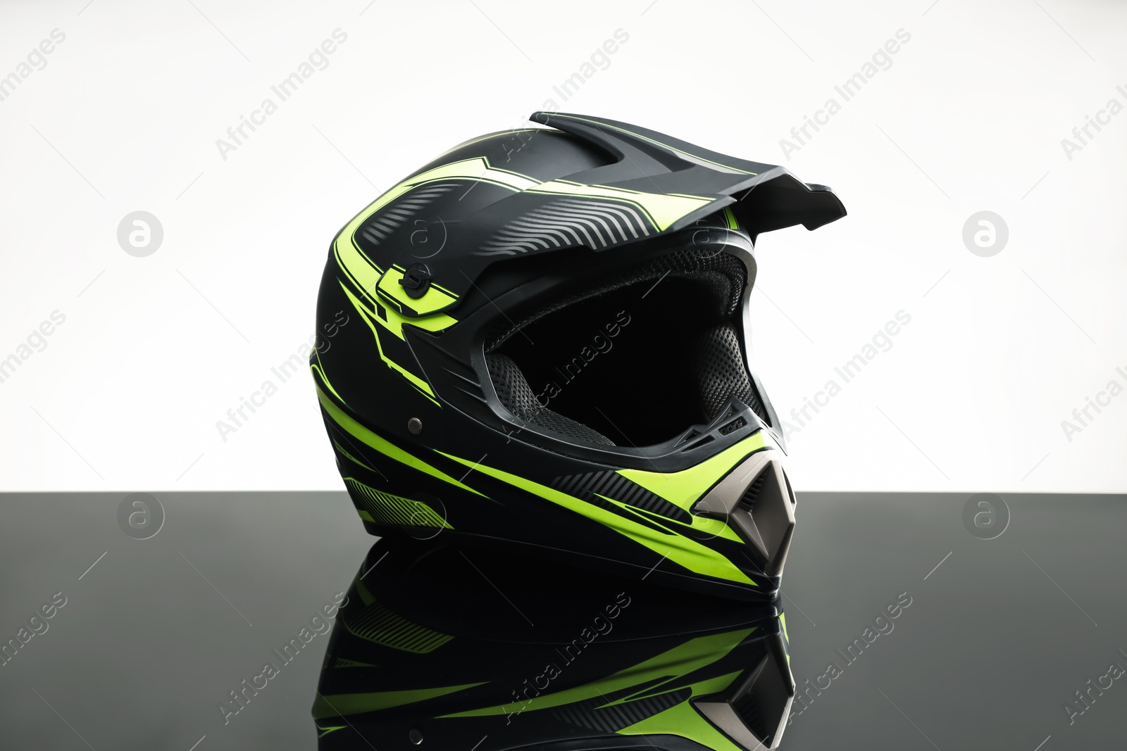 Photo of Modern motorcycle helmet with visor on mirror surface against light grey background