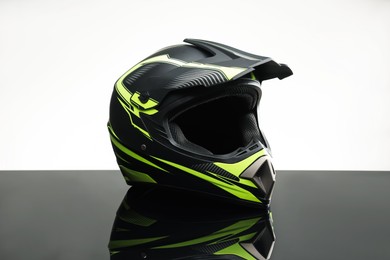 Photo of Modern motorcycle helmet with visor on mirror surface against light grey background