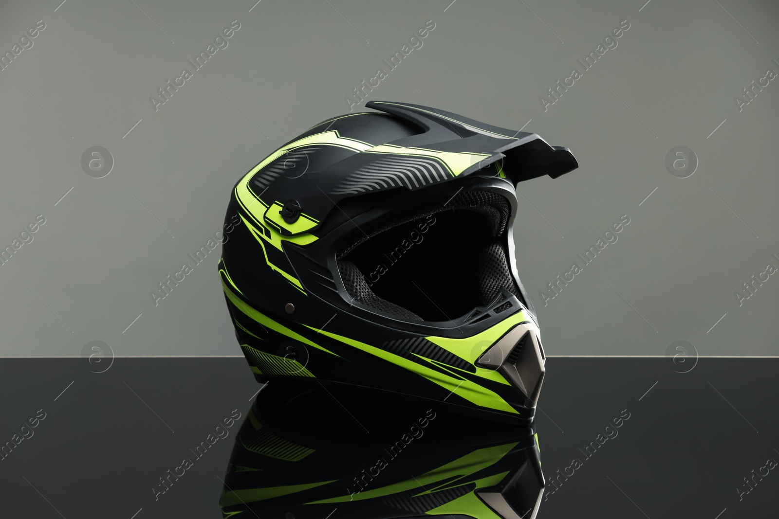 Photo of Modern motorcycle helmet with visor on mirror surface against light grey background