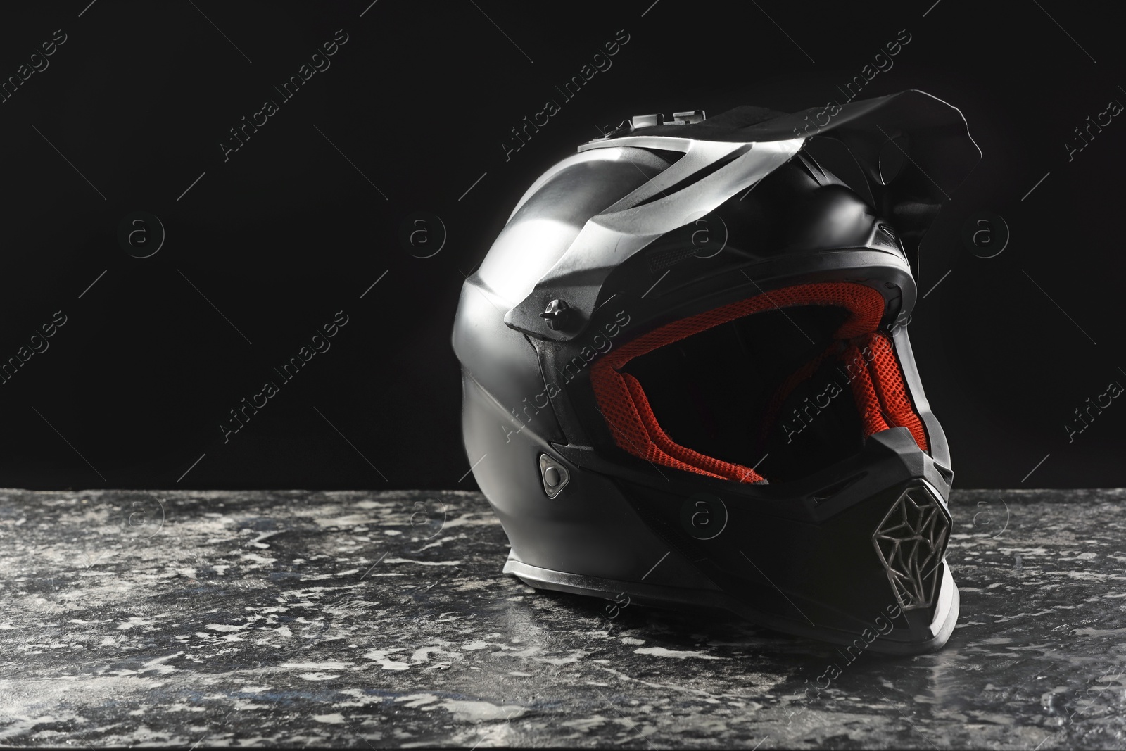 Photo of Modern motorcycle helmet with visor on grey stone surface against black background. Space for text