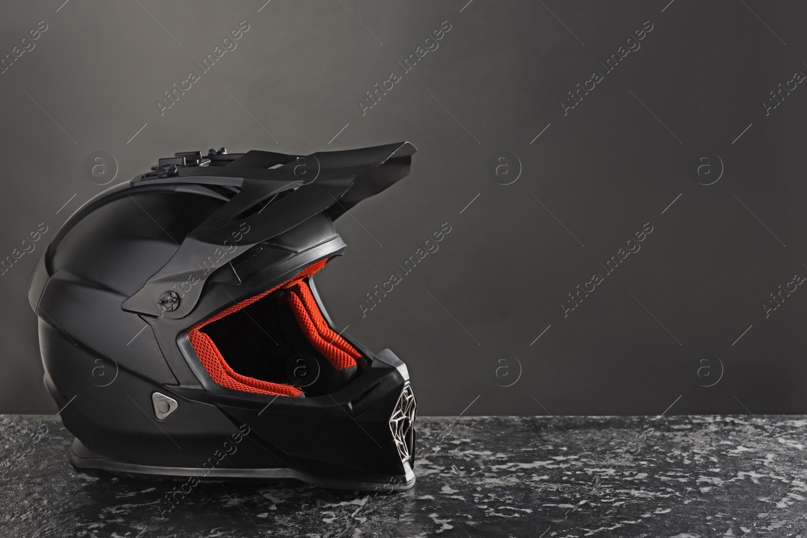 Photo of Modern motorcycle helmet with visor on grey stone surface against black background. Space for text