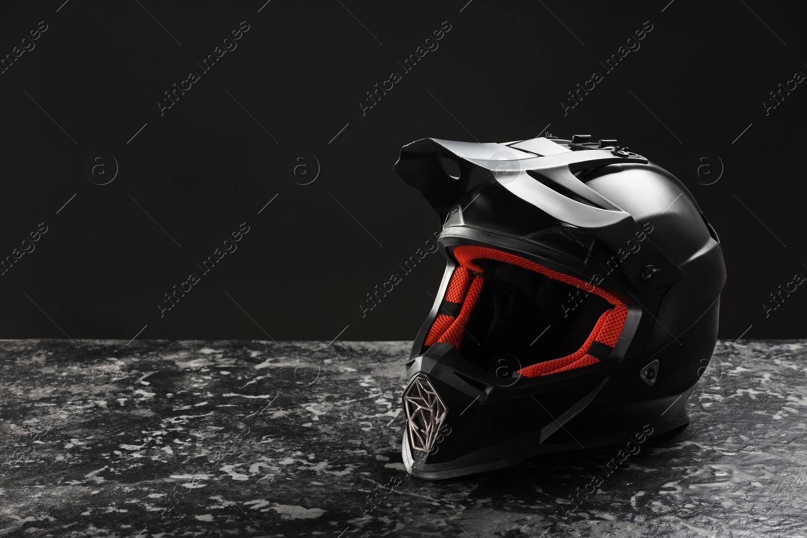 Photo of Modern motorcycle helmet with visor on grey stone surface against black background. Space for text