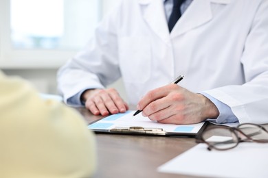 Photo of Doctor writing prescription for patient at wooden table in clinic, closeup