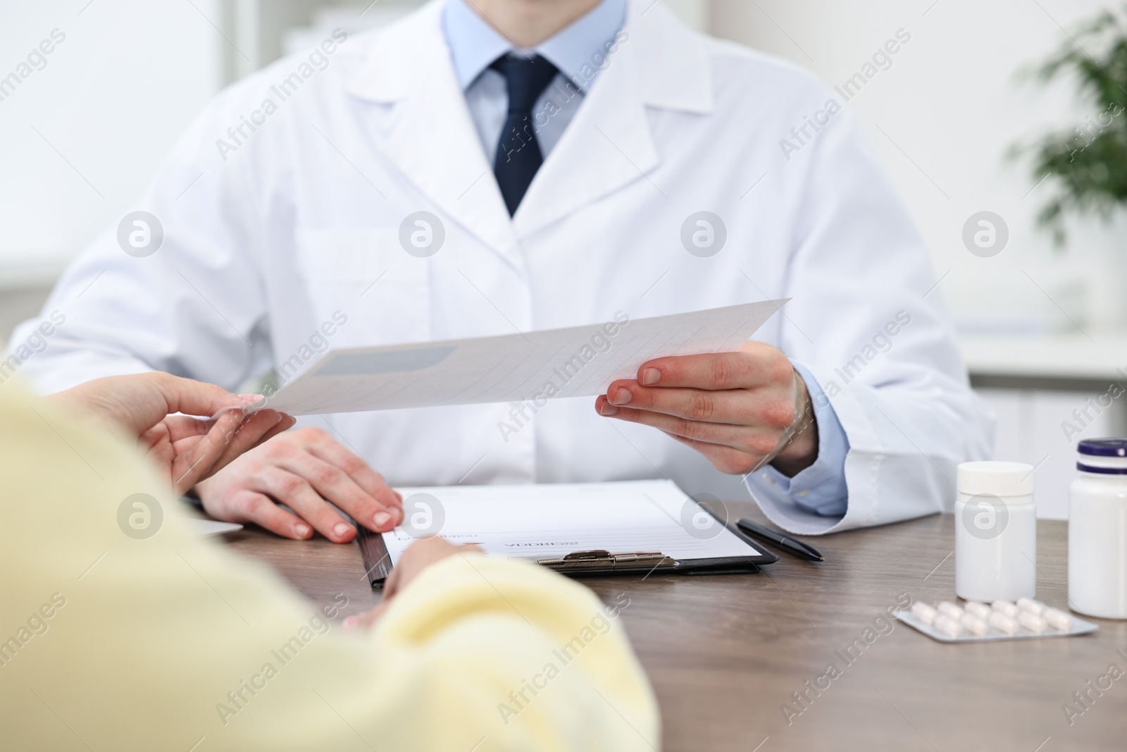 Photo of Doctor giving prescription to patient at wooden table in clinic, closeup