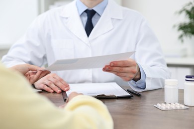 Photo of Doctor giving prescription to patient at wooden table in clinic, closeup