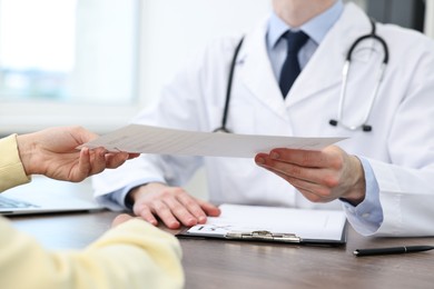 Photo of Doctor giving prescription to patient at wooden table in clinic, closeup