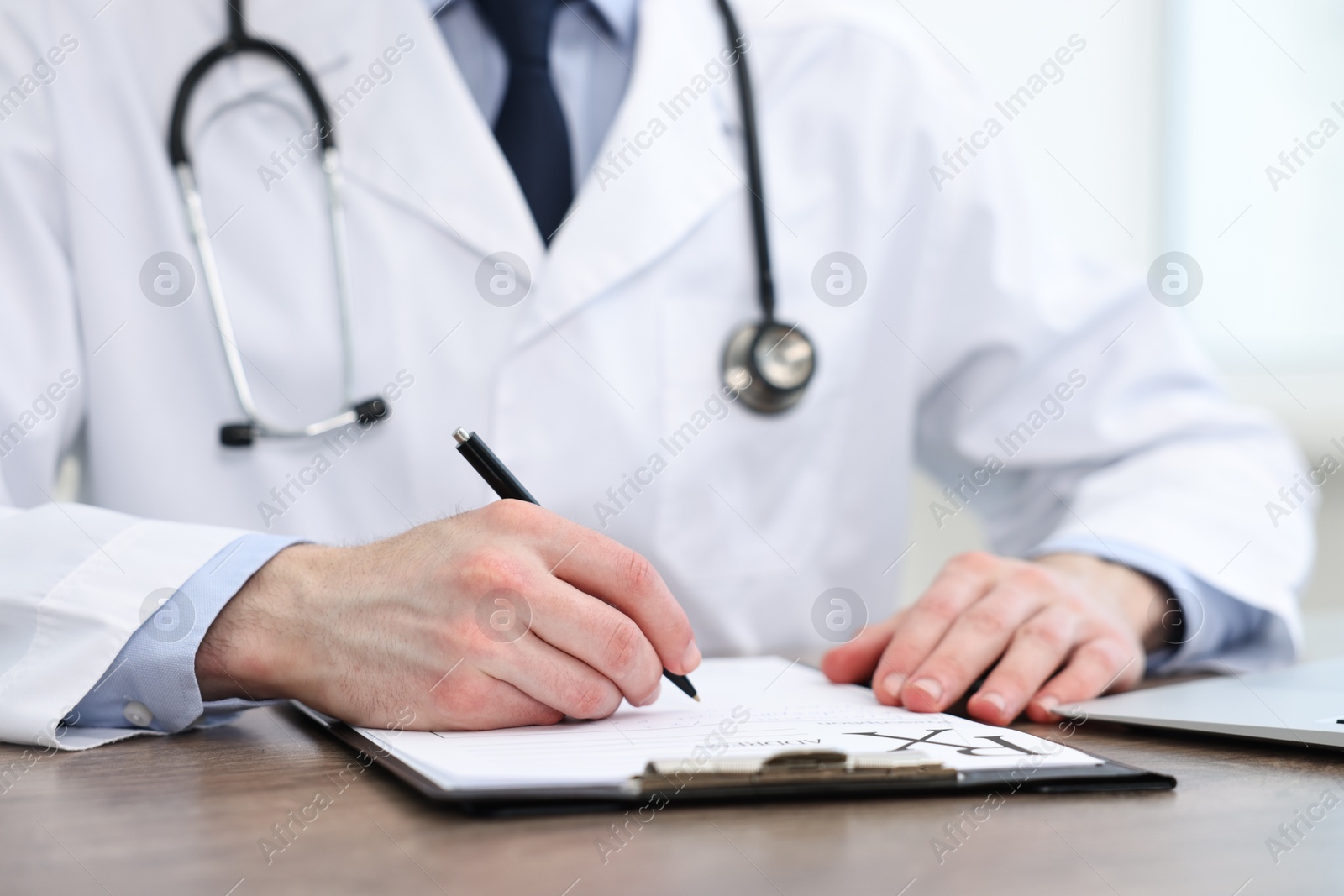 Photo of Doctor writing prescription at wooden table in clinic, closeup