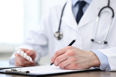 Photo of Doctor with pills writing prescription at wooden table in clinic, closeup