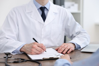 Photo of Doctor writing prescription for patient at wooden table in clinic, closeup