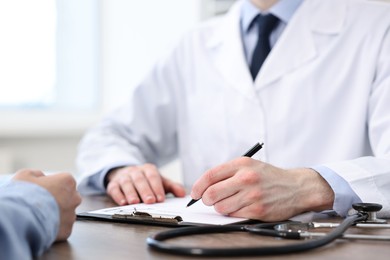 Photo of Doctor writing prescription for patient at wooden table in clinic, closeup