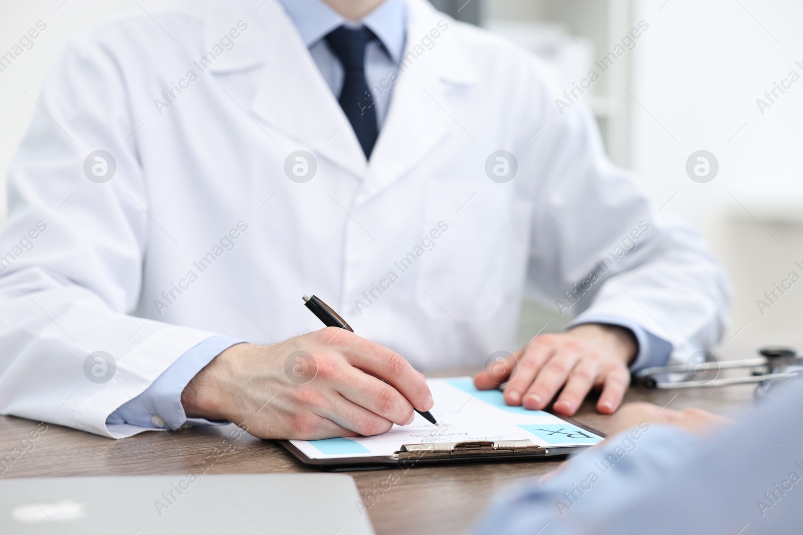 Photo of Doctor writing prescription for patient at wooden table in clinic, closeup