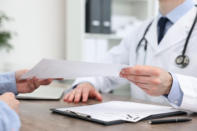 Photo of Doctor giving prescription to patient at wooden table in clinic, closeup