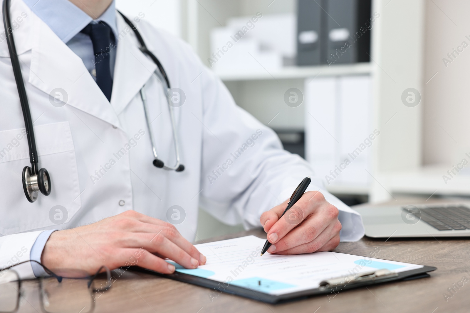 Photo of Doctor writing prescription at wooden table in clinic, closeup