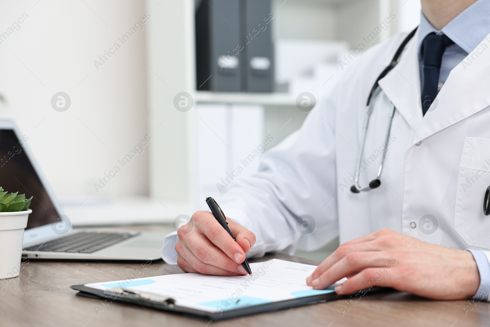 Photo of Doctor writing prescription at wooden table in clinic, closeup