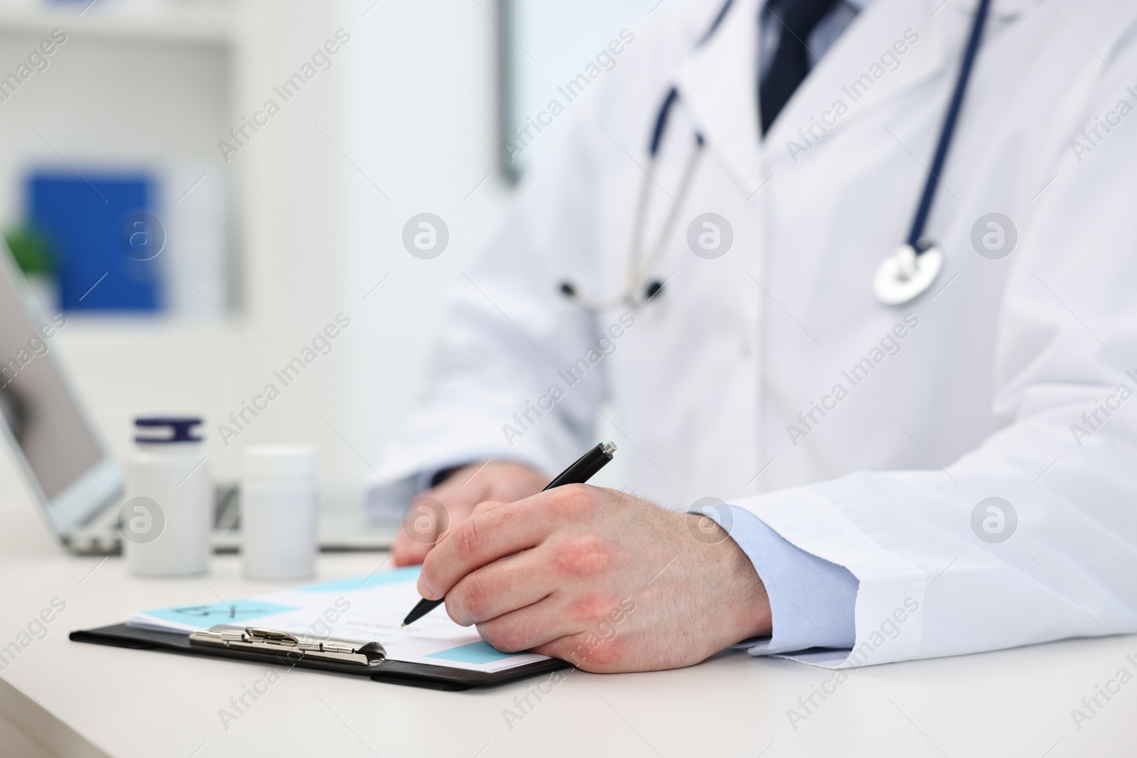 Photo of Doctor writing prescription at white table in clinic, closeup