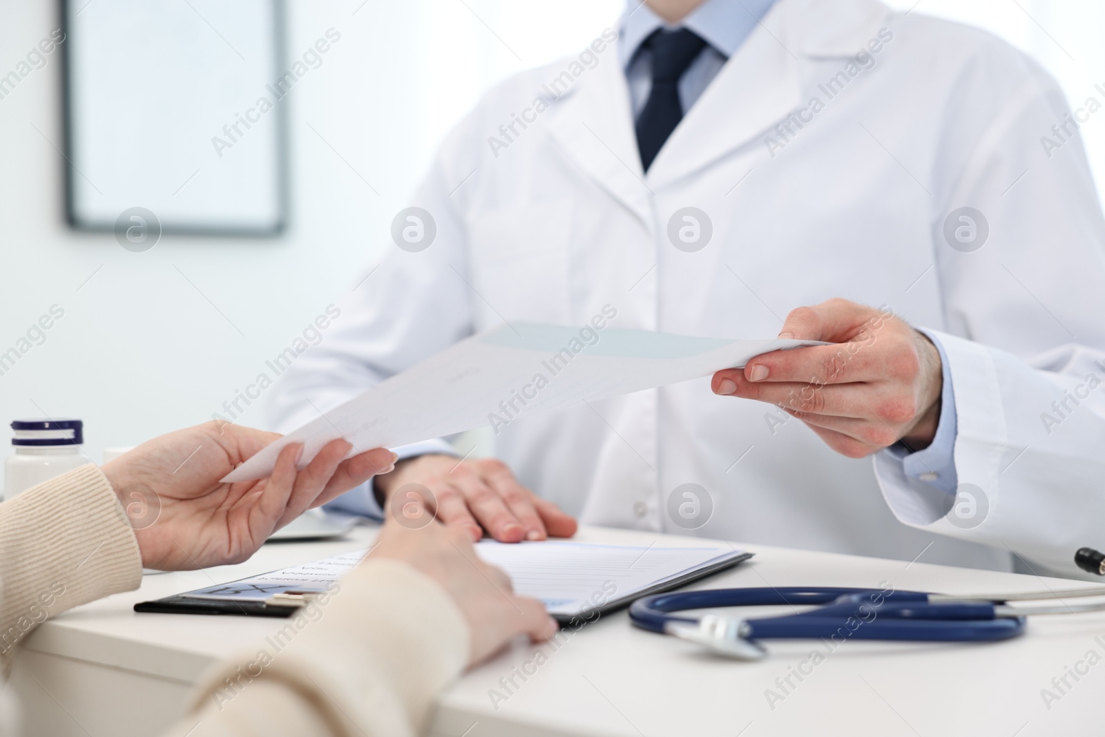 Photo of Doctor giving prescription to patient at white table in clinic, closeup