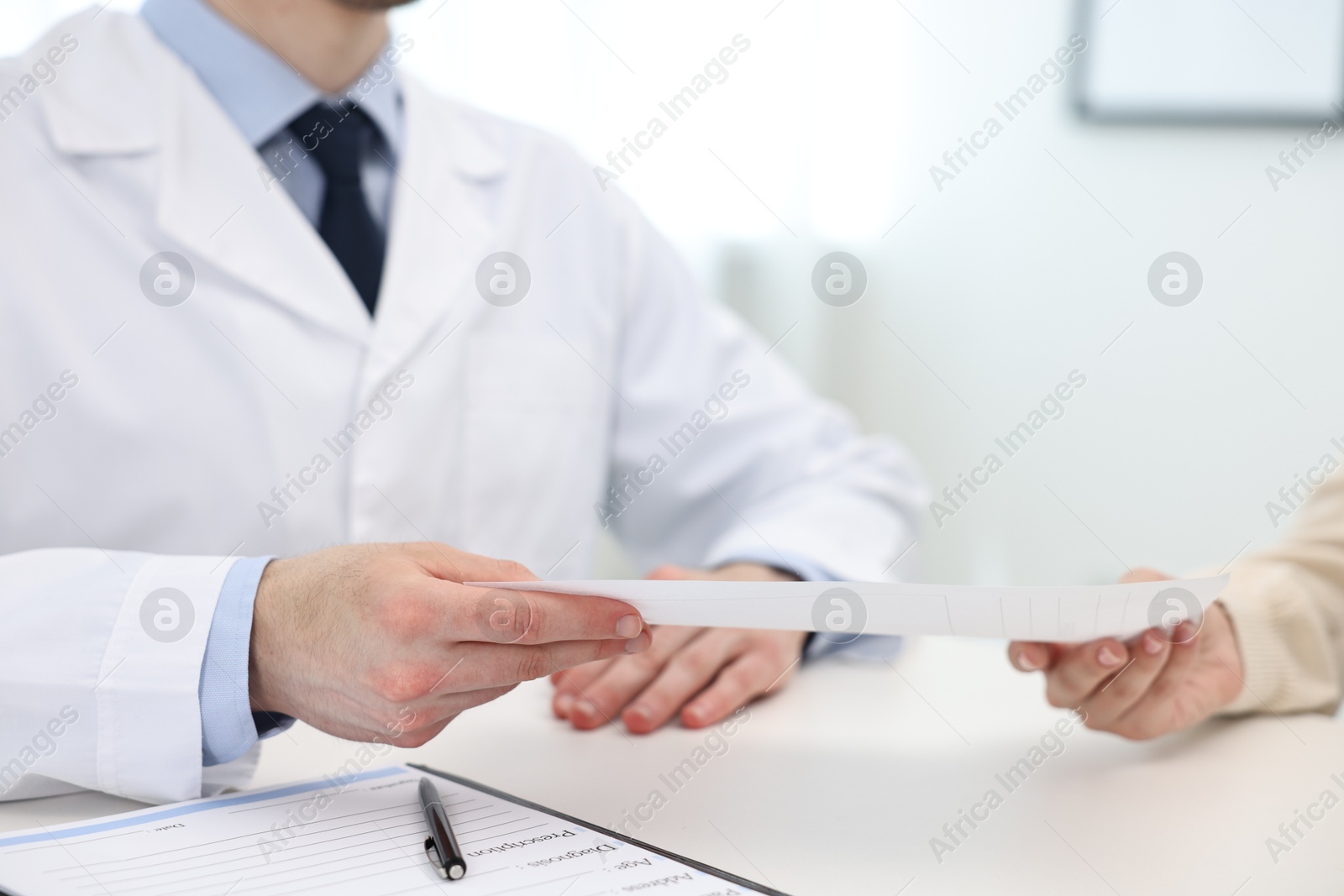 Photo of Doctor giving prescription to patient at white table in clinic, closeup