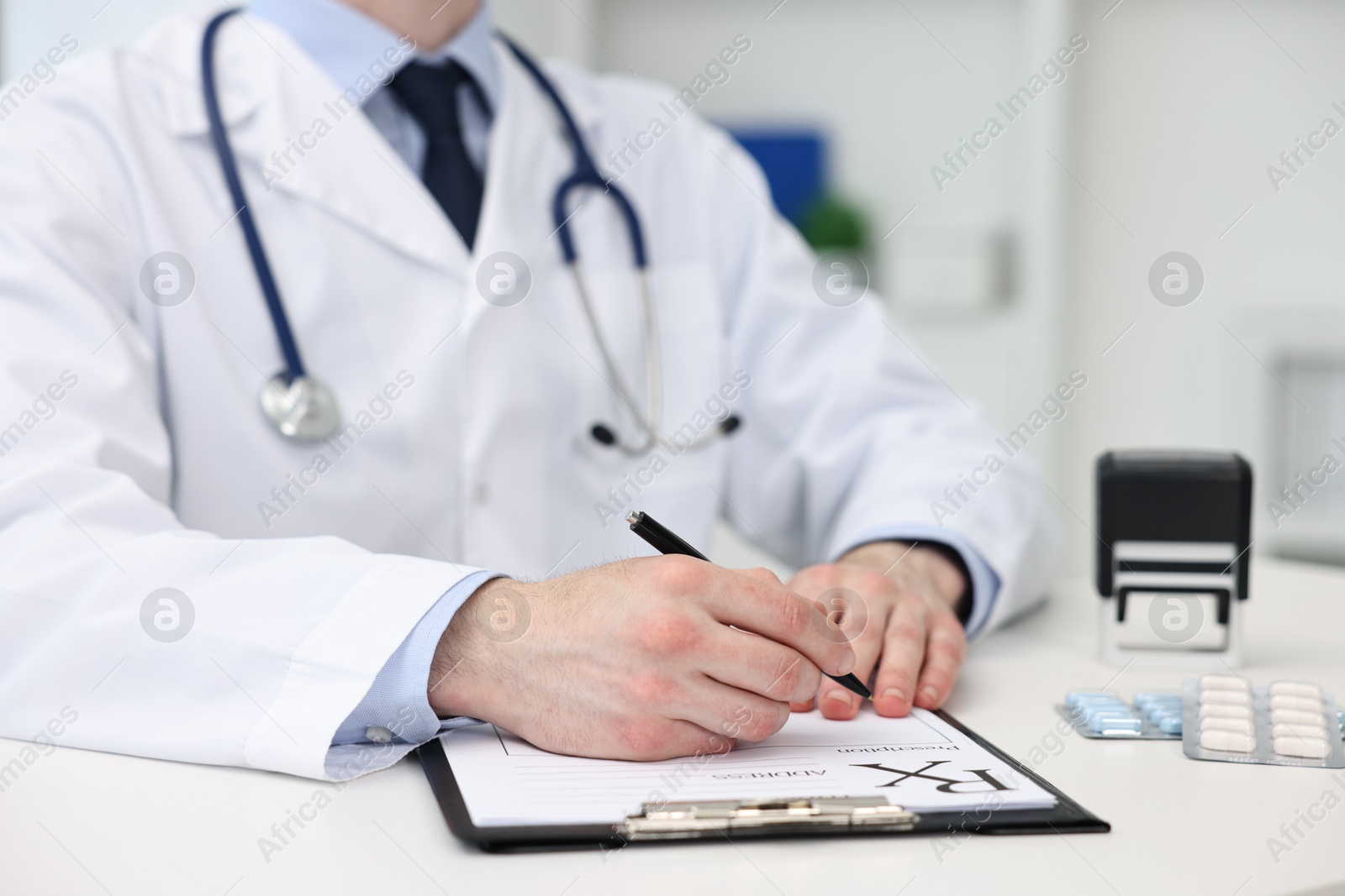 Photo of Doctor writing prescription at white table in clinic, closeup