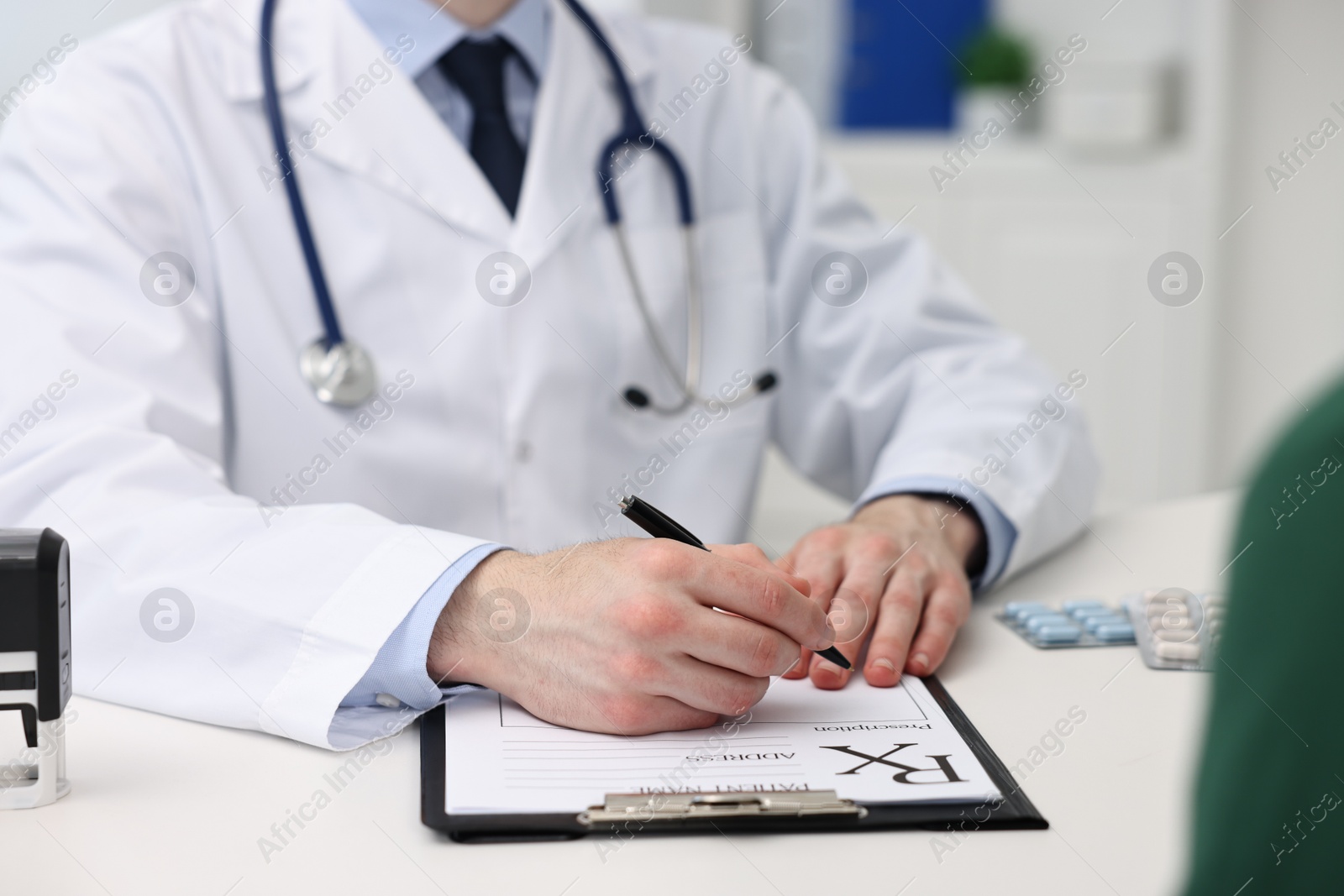 Photo of Doctor writing prescription at white table in clinic, closeup