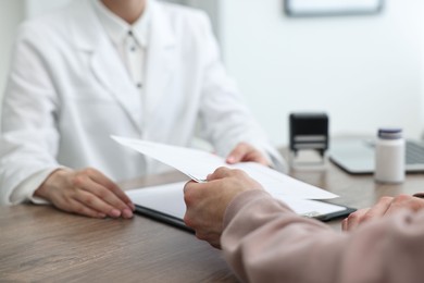 Photo of Doctor giving prescription to patient at wooden table in clinic, closeup