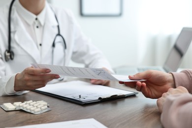 Photo of Doctor giving prescription to patient at wooden table in clinic, closeup