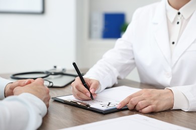 Photo of Doctor writing prescription for patient at wooden table in clinic, closeup