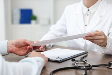 Photo of Doctor giving prescription to patient at wooden table in clinic, closeup